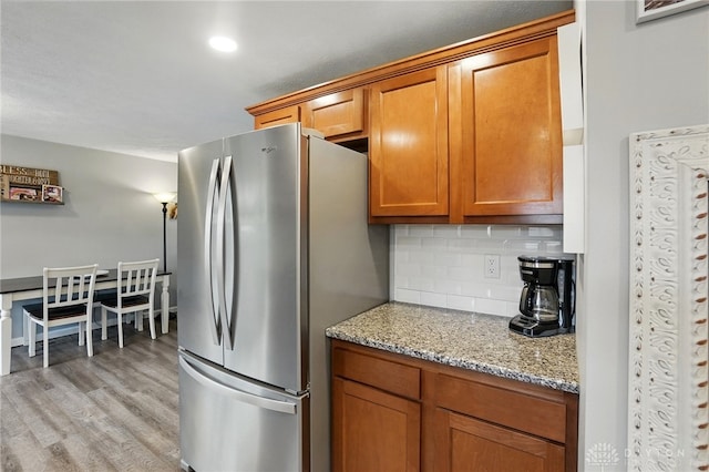 kitchen featuring freestanding refrigerator, brown cabinetry, decorative backsplash, light wood-style floors, and recessed lighting