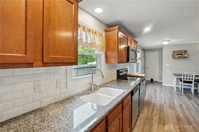 kitchen with a sink, stainless steel appliances, brown cabinetry, tasteful backsplash, and light wood finished floors
