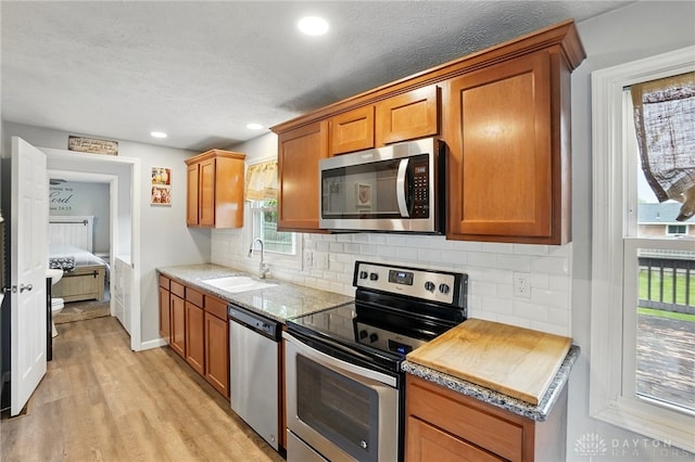 kitchen with appliances with stainless steel finishes, a sink, light wood-type flooring, backsplash, and brown cabinetry
