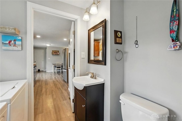 bathroom featuring wood finished floors, vanity, toilet, independent washer and dryer, and recessed lighting
