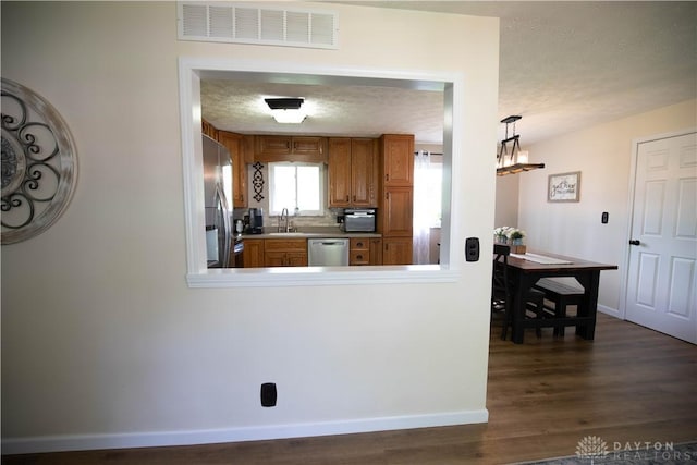 kitchen with stainless steel appliances, dark wood-style floors, brown cabinetry, baseboards, and a textured ceiling