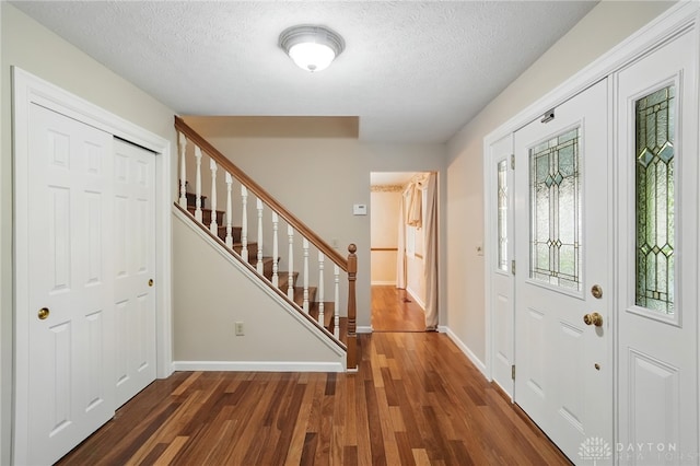 foyer entrance featuring wood finished floors, stairway, a textured ceiling, and baseboards