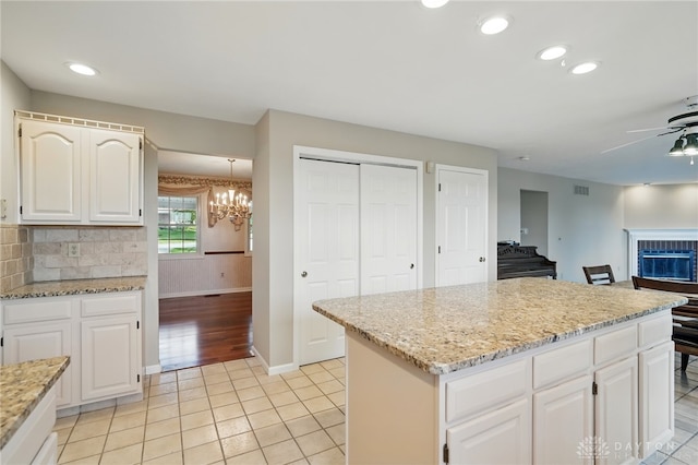 kitchen with a ceiling fan, a chandelier, light stone counters, baseboards, and white cabinetry