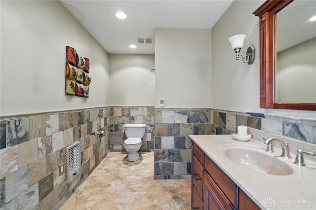 bathroom with toilet, a wainscoted wall, tile walls, vanity, and recessed lighting