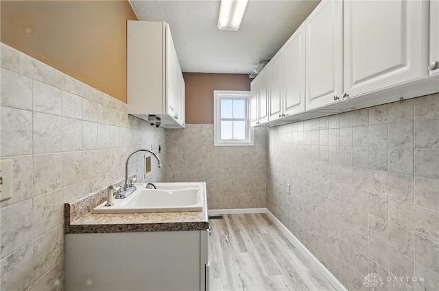 laundry area featuring a sink, light wood finished floors, tile walls, and wainscoting