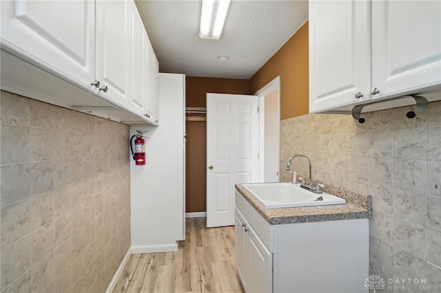2337 Eastwind Dr, Beavercreek, OH 45434 - laundry area with a sink, tile walls, light wood finished floors, and baseboards