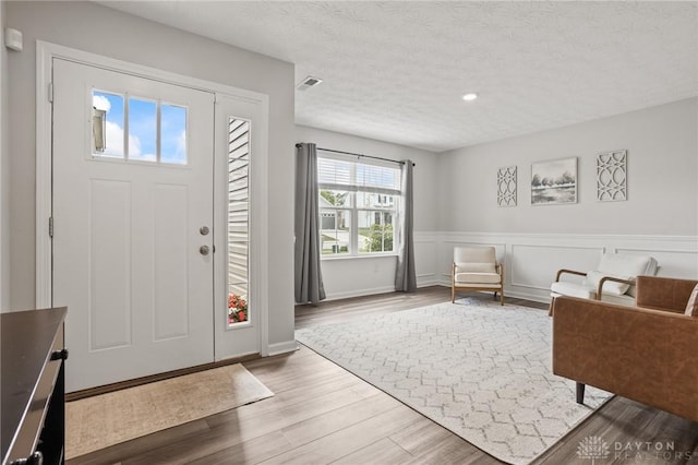 foyer entrance featuring wood finished floors, a textured ceiling, a wainscoted wall, and recessed lighting