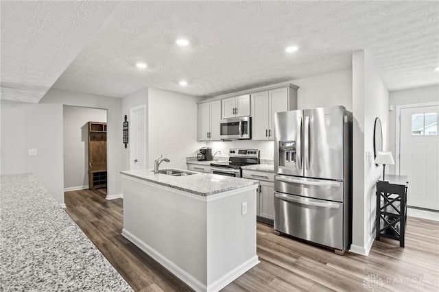 kitchen featuring appliances with stainless steel finishes, a sink, wood finished floors, baseboards, and a textured ceiling
