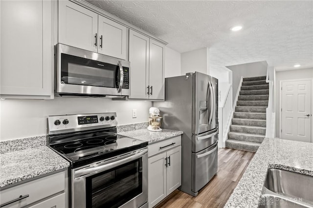 kitchen with appliances with stainless steel finishes, light wood-type flooring, light stone counters, a textured ceiling, and recessed lighting
