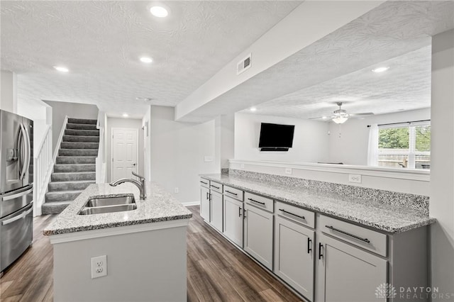 kitchen with a sink, stainless steel refrigerator with ice dispenser, a textured ceiling, a kitchen island with sink, and a ceiling fan