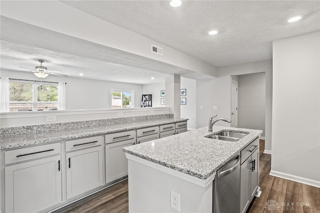 kitchen with a sink, stainless steel dishwasher, dark wood finished floors, a center island with sink, and a textured ceiling