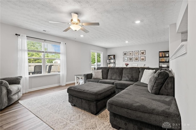 living area featuring wood finished floors, a ceiling fan, a textured ceiling, baseboards, and recessed lighting
