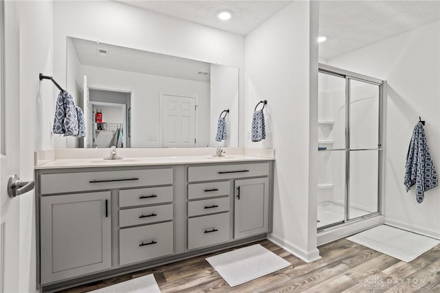 bathroom with a stall shower, wood finished floors, double vanity, a textured ceiling, and baseboards