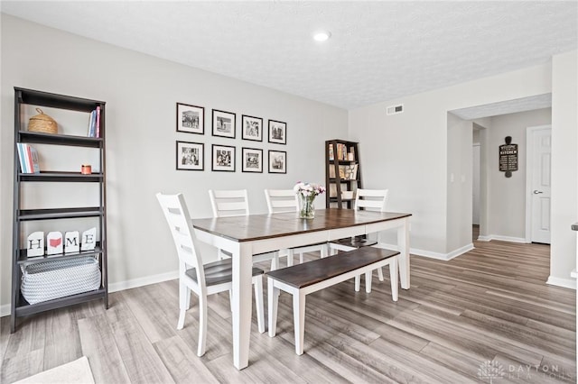 dining room with light wood finished floors, baseboards, a textured ceiling, and recessed lighting