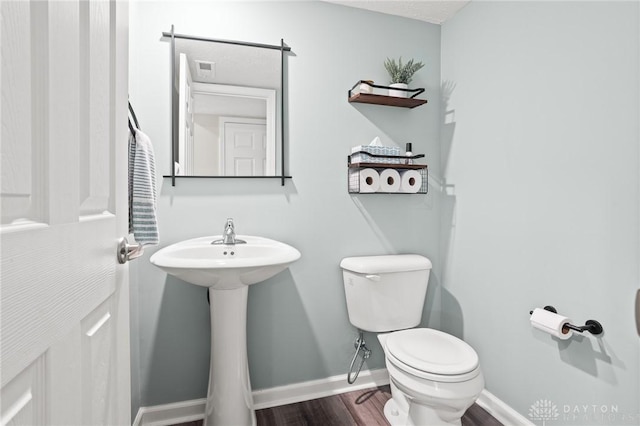 bathroom with toilet, wood finished floors, baseboards, and a sink