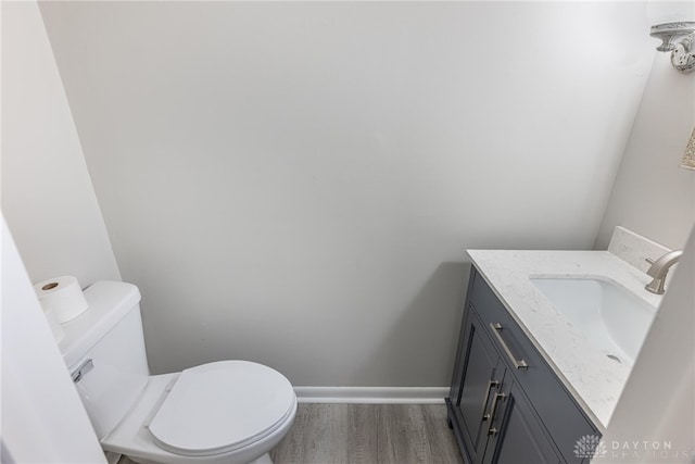 half bath featuring vanity, wood finished floors, toilet, and baseboards