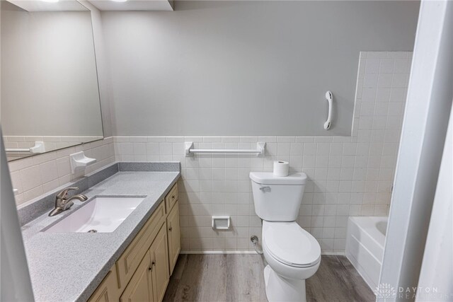 bathroom featuring wood finished floors, tile walls, toilet, vanity, and a bathtub