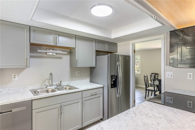 kitchen featuring stainless steel appliances, a sink, gray cabinetry, and a raised ceiling
