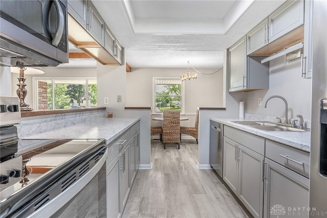 kitchen with stainless steel appliances, gray cabinets, a sink, and light wood-style flooring