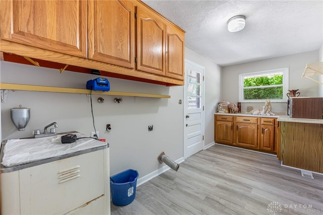 laundry area featuring cabinet space, light wood-style floors, a textured ceiling, baseboards, and hookup for a washing machine
