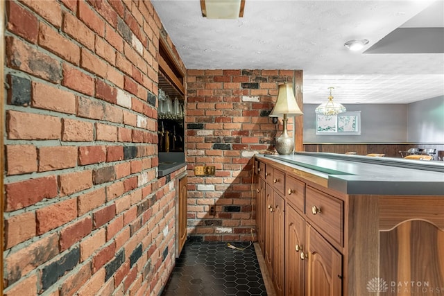 kitchen with brick wall, brown cabinetry, and dark tile patterned floors
