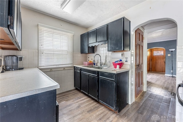 57 W Maplewood Ave, Dayton, OH 45405 - kitchen featuring arched walkways, light wood-style flooring, dark cabinets, a textured ceiling, and light countertops