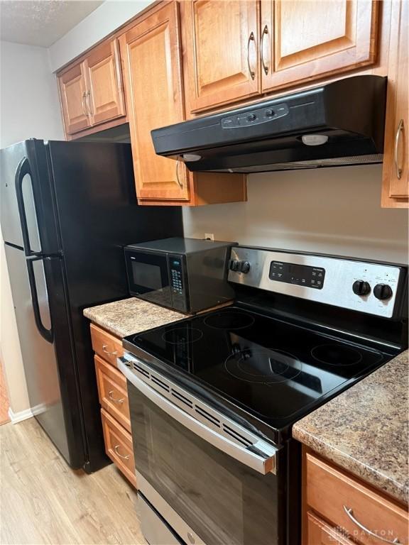 1109 Arrowhead Xing Unit A, West Carrollton, OH 45449 - kitchen featuring electric stove, under cabinet range hood, black microwave, light wood-type flooring, and light stone counters