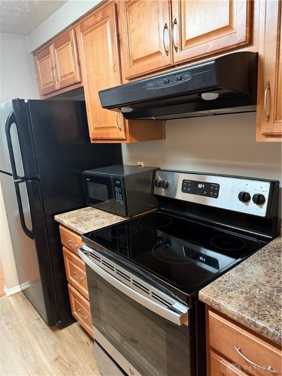 1109 Arrowhead Xing Unit A, West Carrollton, OH 45449 - kitchen featuring black appliances, under cabinet range hood, light wood-type flooring, light stone countertops, and brown cabinets