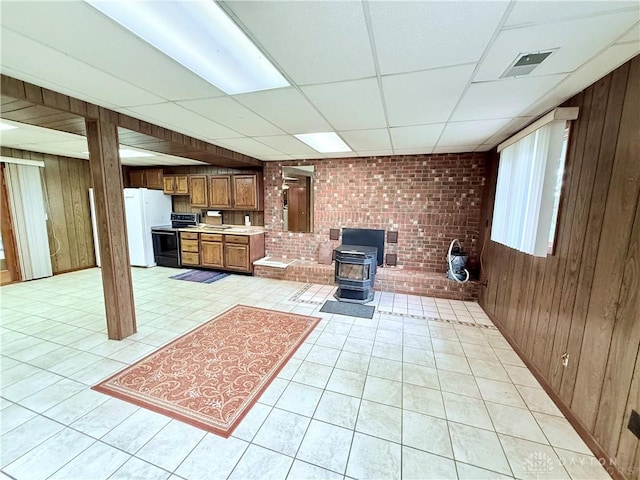 5778 Cedarwood Dr, Lewisburg, OH 45338 - unfurnished living room featuring a drop ceiling, a wood stove, wood walls, light tile patterned flooring, and brick wall