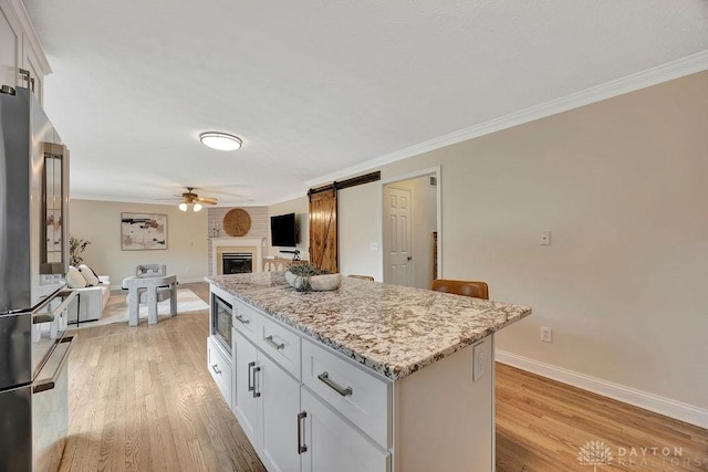 406 Forge Dr, Lebanon, OH 45036 - kitchen with stainless steel appliances, ceiling fan, a kitchen island, light wood finished floors, and a large fireplace