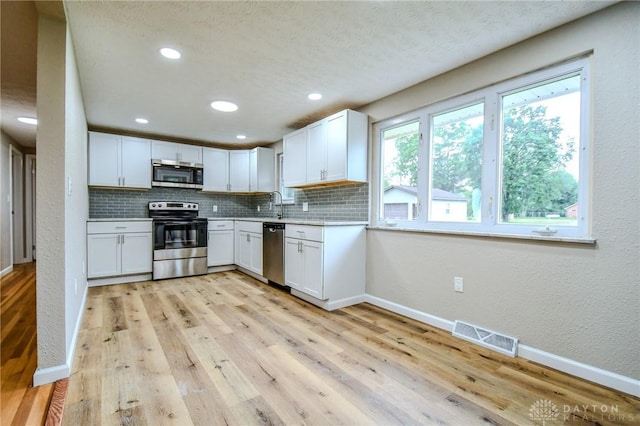 3653 Cloverdale Rd, Medway, OH 45341 - kitchen featuring stainless steel appliances, decorative backsplash, white cabinets, light countertops, and light wood-type flooring