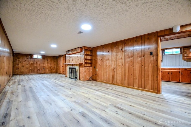 3653 Cloverdale Rd, Medway, OH 45341 - unfurnished living room with wood walls, light wood-style flooring, a brick fireplace, plenty of natural light, and a textured ceiling