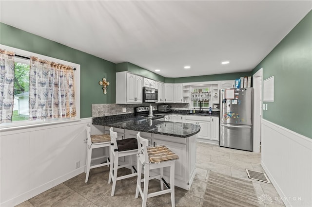 1012 W Sparrow Rd, Springfield, OH 45502 - kitchen featuring appliances with stainless steel finishes, a peninsula, a wainscoted wall, white cabinets, and a kitchen bar