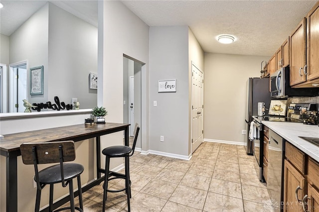1690 Piper Ln Unit 206, Washington Twp, OH 45440 - kitchen featuring brown cabinetry, stainless steel appliances, a textured ceiling, light tile patterned floors, and light countertops