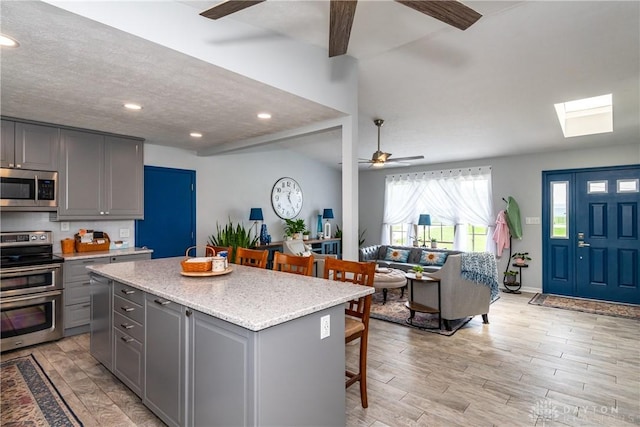 9673 Dayton Greenville Pike, Brookville, OH 45309 - kitchen featuring stainless steel appliances, ceiling fan, gray cabinets, a kitchen bar, and light wood finished floors