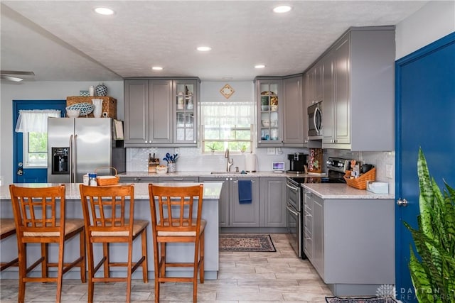 9673 Dayton Greenville Pike, Brookville, OH 45309 - kitchen featuring appliances with stainless steel finishes, gray cabinetry, a breakfast bar, decorative backsplash, and a sink