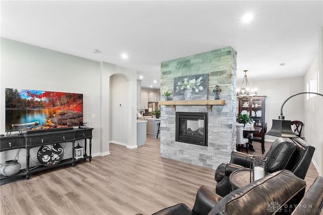 4978 Renaissance Park Dr, Middletown, OH 45005 - living room featuring baseboards, a stone fireplace, light wood-style flooring, arched walkways, and a chandelier