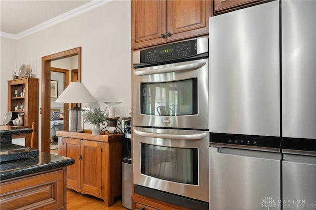 1134 N Webb Rd, Adams Twp, OH 45177 - kitchen featuring appliances with stainless steel finishes, crown molding, brown cabinetry, light wood-style flooring, and dark stone countertops