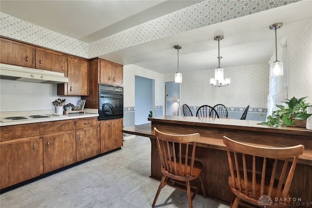 300 Magnolia Ave, Englewood, OH 45322 - kitchen with wallpapered walls, black oven, under cabinet range hood, a chandelier, and decorative light fixtures