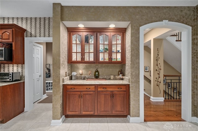 7607 Stone Ridge Dr, Springboro, OH 45066 - kitchen featuring stainless steel microwave, glass insert cabinets, light tile patterned flooring, baseboards, and arched walkways