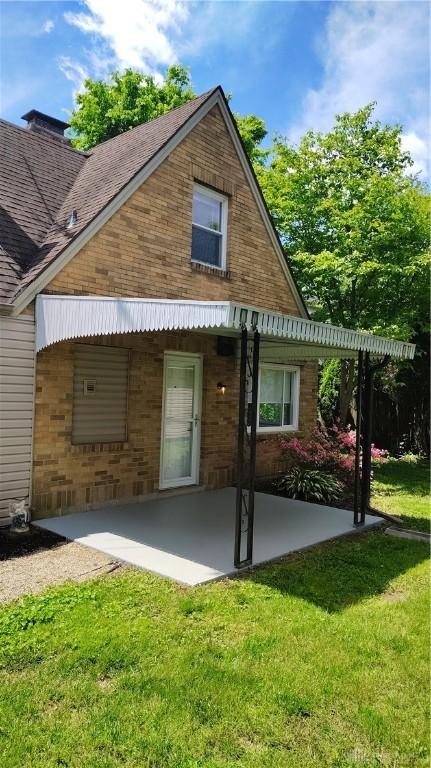 413 W Lake Ave, New Carlisle, OH 45344 - rear view of property featuring a patio area, a yard, and brick siding