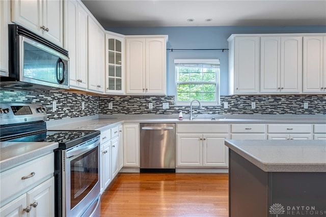 6265 Amberley Ct, Liberty Twp, OH 45044 - kitchen featuring appliances with stainless steel finishes, a sink, light countertops, decorative backsplash, and glass insert cabinets