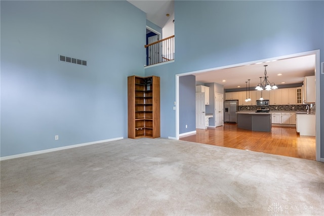 6265 Amberley Ct, Liberty Twp, OH 45044 - unfurnished living room featuring light colored carpet, a chandelier, a high ceiling, baseboards, and recessed lighting