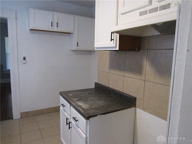 2455 Catalpa Dr, Dayton, OH 45406 - kitchen with under cabinet range hood, dark countertops, white cabinets, light tile patterned floors, and backsplash