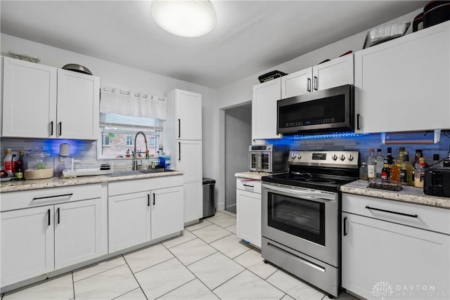 2819 Mccall St, Dayton, OH 45417 - kitchen featuring stainless steel appliances, decorative backsplash, a sink, white cabinets, and light tile patterned floors