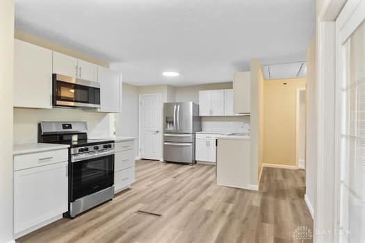 1108 Donson Dr, Kettering, OH 45429 - kitchen with appliances with stainless steel finishes, light countertops, white cabinets, and light wood finished floors