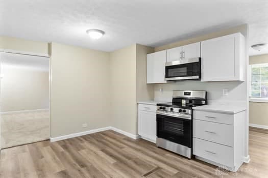 1108 Donson Dr, Kettering, OH 45429 - kitchen with stainless steel appliances, light wood-style flooring, light countertops, baseboards, and white cabinets