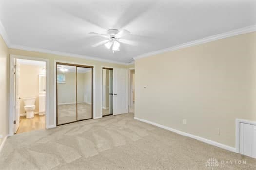 1108 Donson Dr, Kettering, OH 45429 - unfurnished bedroom with crown molding, two closets, light carpet, baseboards, and connected bathroom