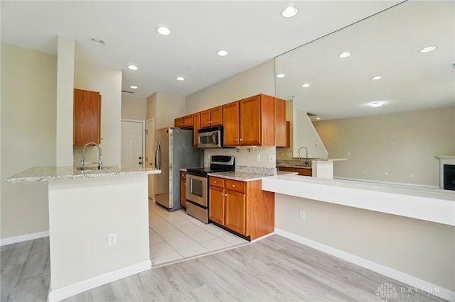 9235 Great Lakes Cir, Washington Twp, OH 45458 - kitchen with appliances with stainless steel finishes, a peninsula, a sink, brown cabinetry, and light wood-style floors