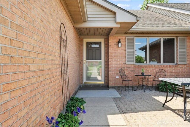 1462 Dee Anne Dr, Xenia, OH 45385 - doorway to property featuring a shingled roof, brick siding, outdoor dining area, and a patio area
